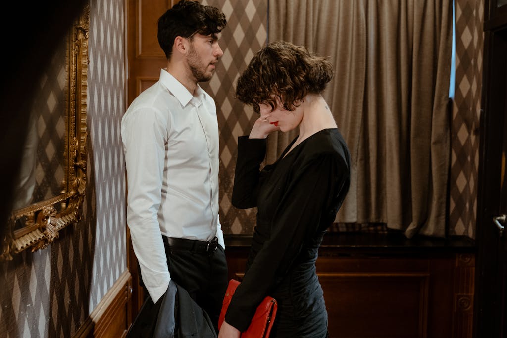 A couple in elegant attire stands in a vintage room with classic decor, expressing emotion.